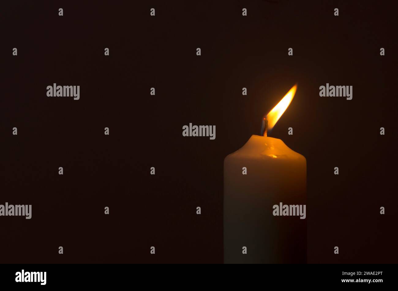 Blurred single burning candle flame or light is glowing on a white ...