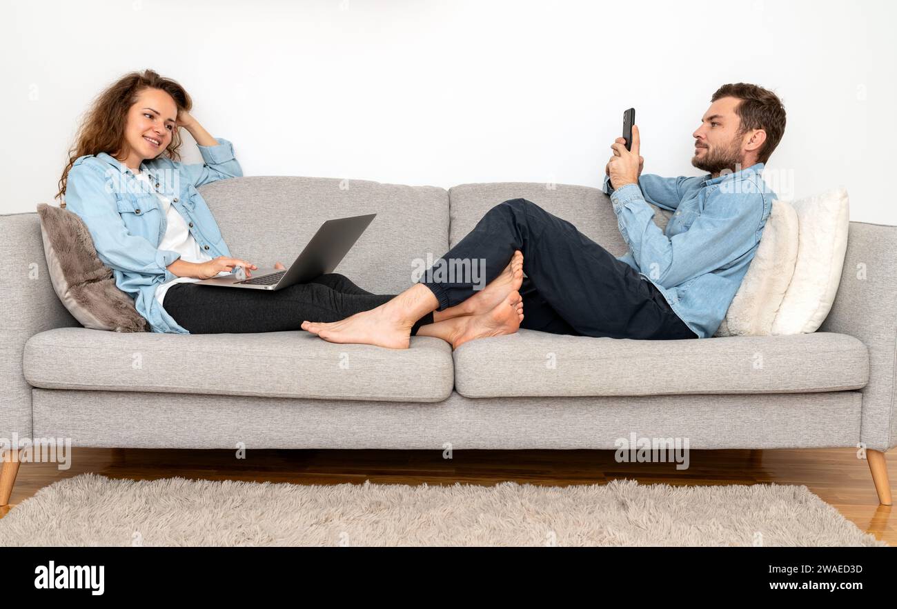Woman and man relax on sofa and using their digital portable information devices. Stock Photo