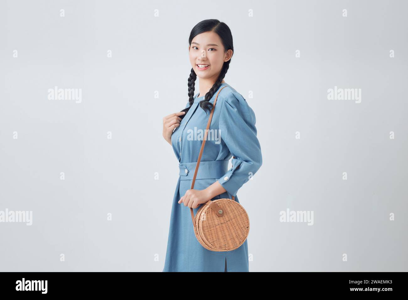 Elegant happy smiling woman wearing trendy denim dress, with small shoulder round wicker bag Stock Photo