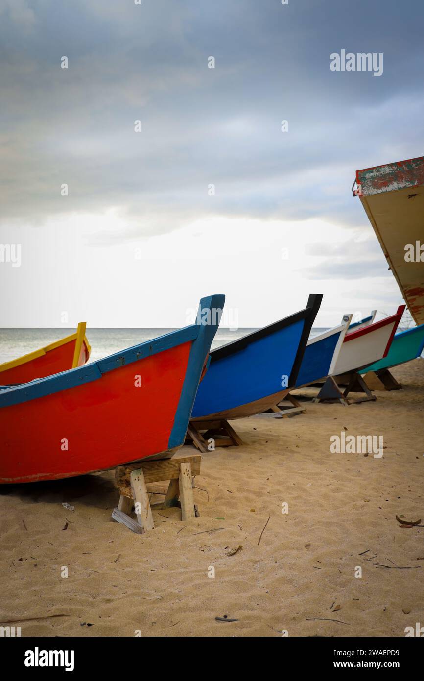 A cluster of fishing boats resting on the sandy shoreline near a destroyed building. Stock Photo