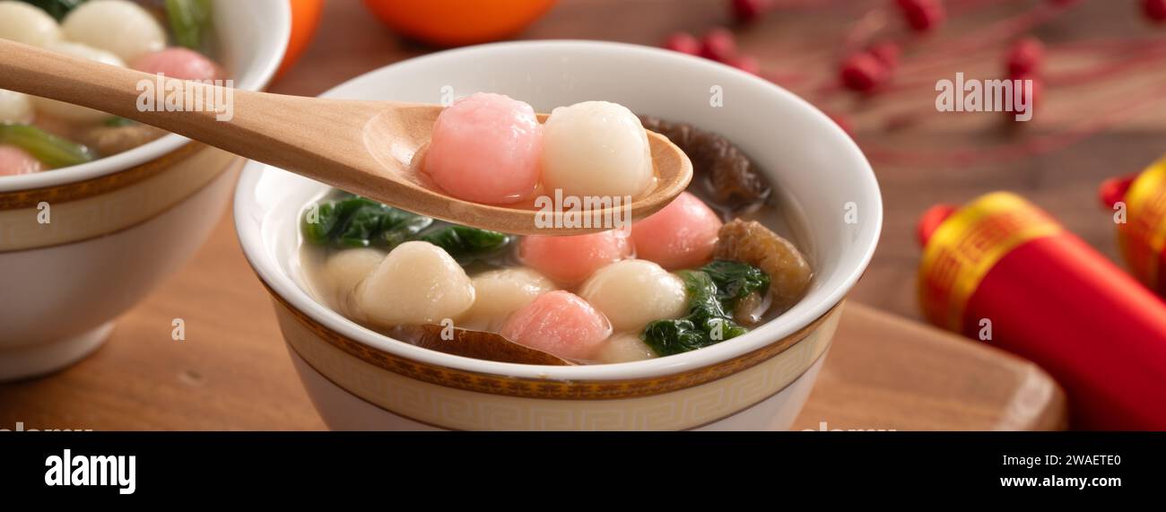 Eating red and white small tangyuan, tang yuan, glutinous rice dumpling balls with savory soup in a bowl on wooden table background for lunar new year Stock Photo