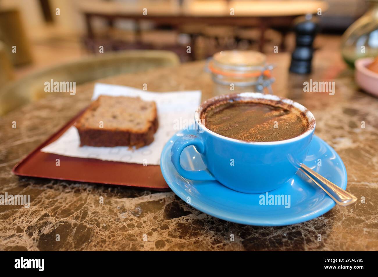 A cup of cappuccino coffee with a slice of cake in a cafe in the UK Stock Photo