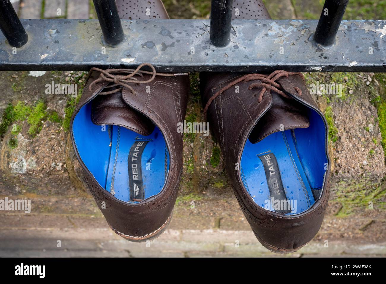 A pair of laced-up, discarded brown shoes are pinned beneath railings in a street at Loughborough Junction, on 3rd January 2024, in London, England. Stock Photo