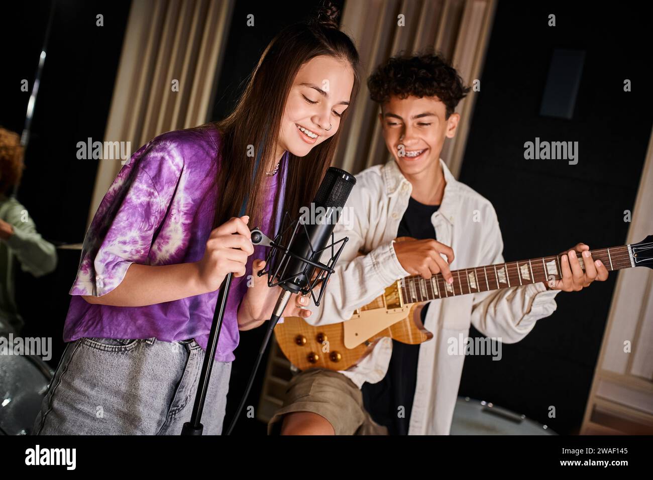 adorable jolly teenage girl singing song next to her friend with braces playing guitar in studio