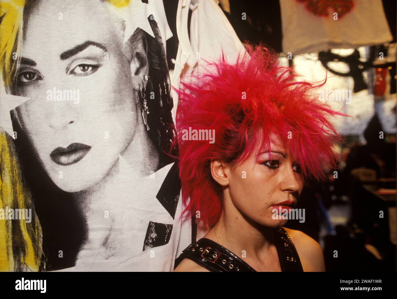 Punk teenage girls shop assistant in Boy at 153  Kings Road, Chelsea boutique, 1980s. Spiky bright red backcombed punk hair and looking mournful, under the poster of Peter Robinson a British Jamaican pop singer; better know as Marilyn, who was at the forefront of the New Romantic movement. Chelsea, London, England 1983 HOMER SYKES Stock Photo