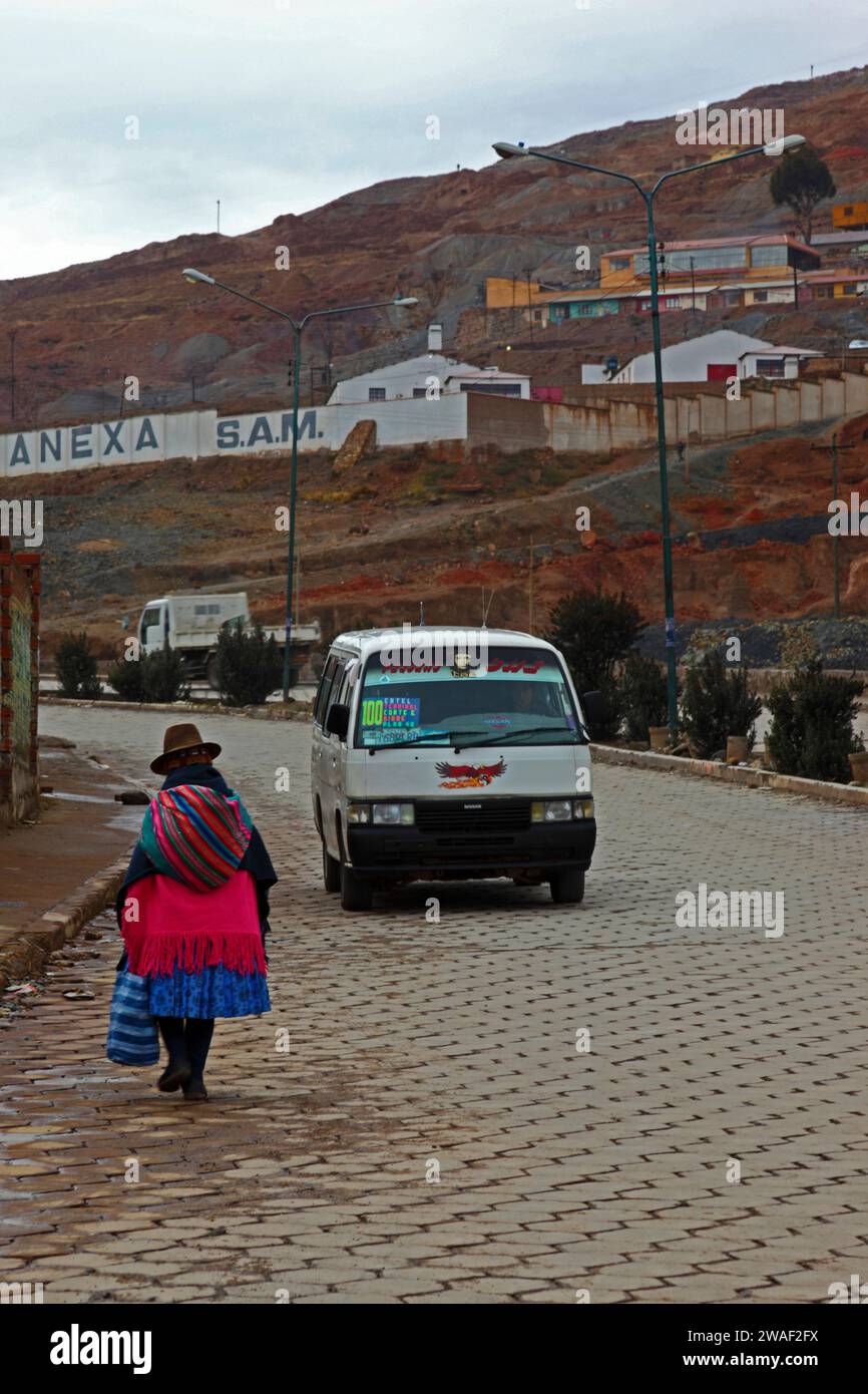 Local Quechua woman wearing traditional dress walking along road at the base of Cerro Rico with past a cooperative mines nearby, Potosi, Bolivia Stock Photo