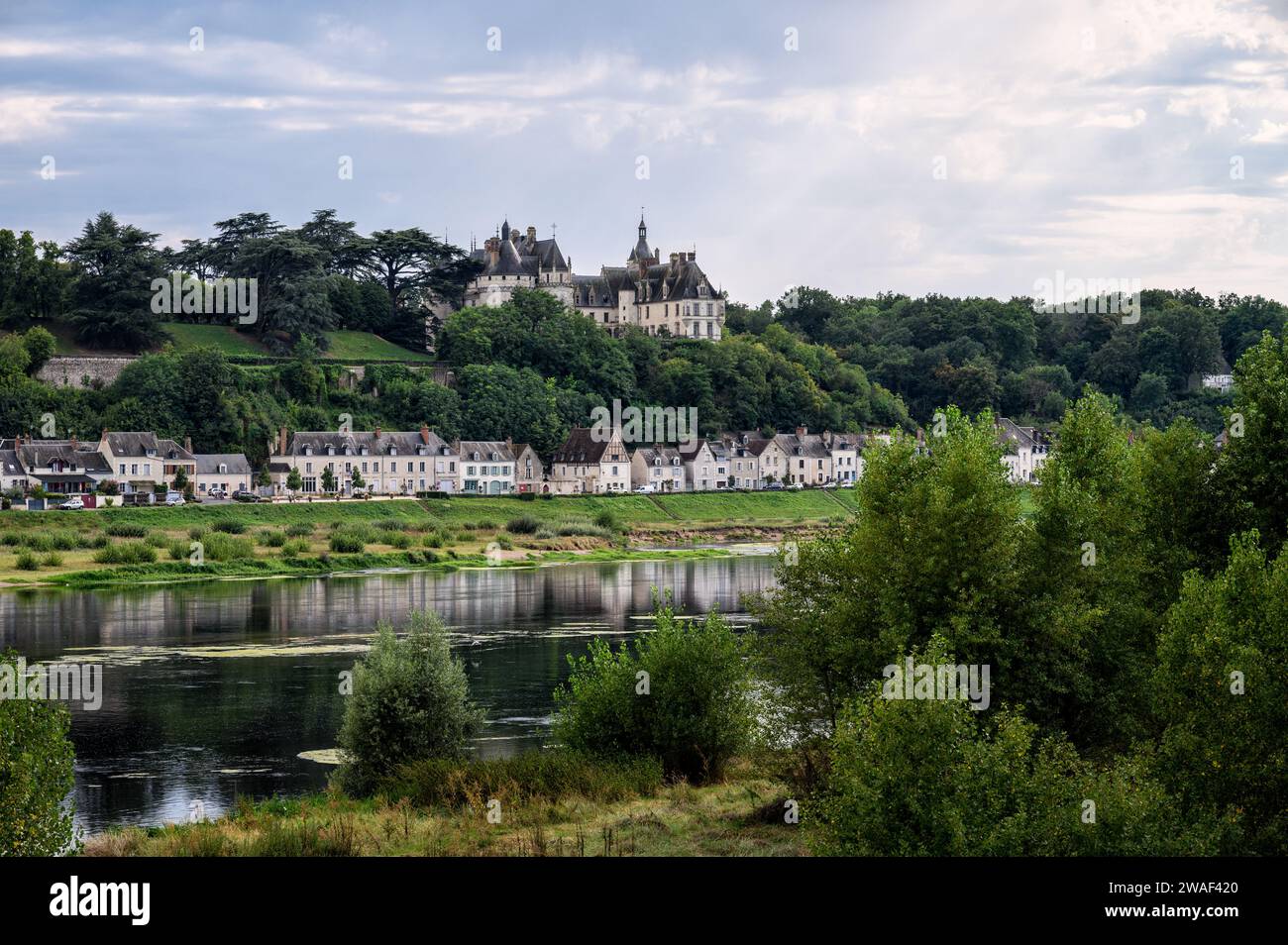 The river Loire as it passes through the village of Amboise with the castle at the top of the mountain surrounded by trees. Stock Photo