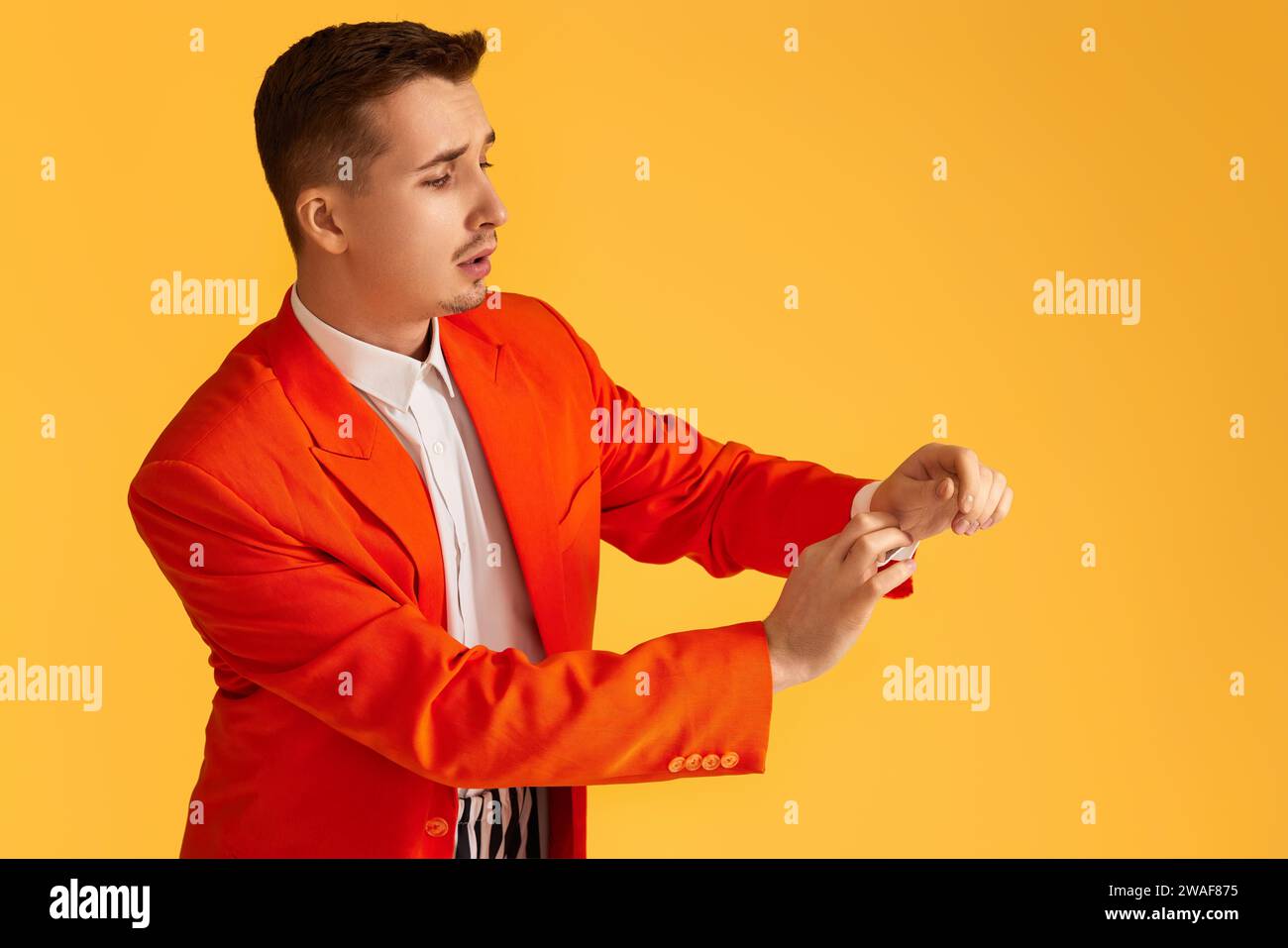 fashionable young man in orange jacket and striped pants on yellow ...