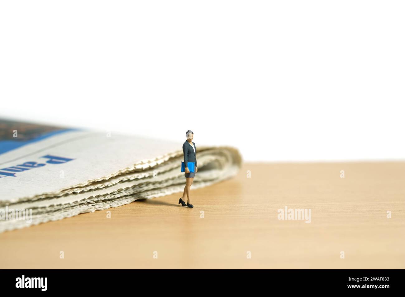 Miniature people toy figure photography. A businesswoman standing walking with newspaper on the desk. Isolated on white background. Image photo Stock Photo