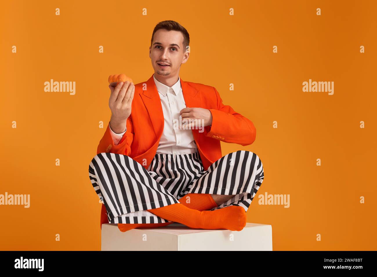 extravagant funny young man in orange jacket and striped pants holding ...