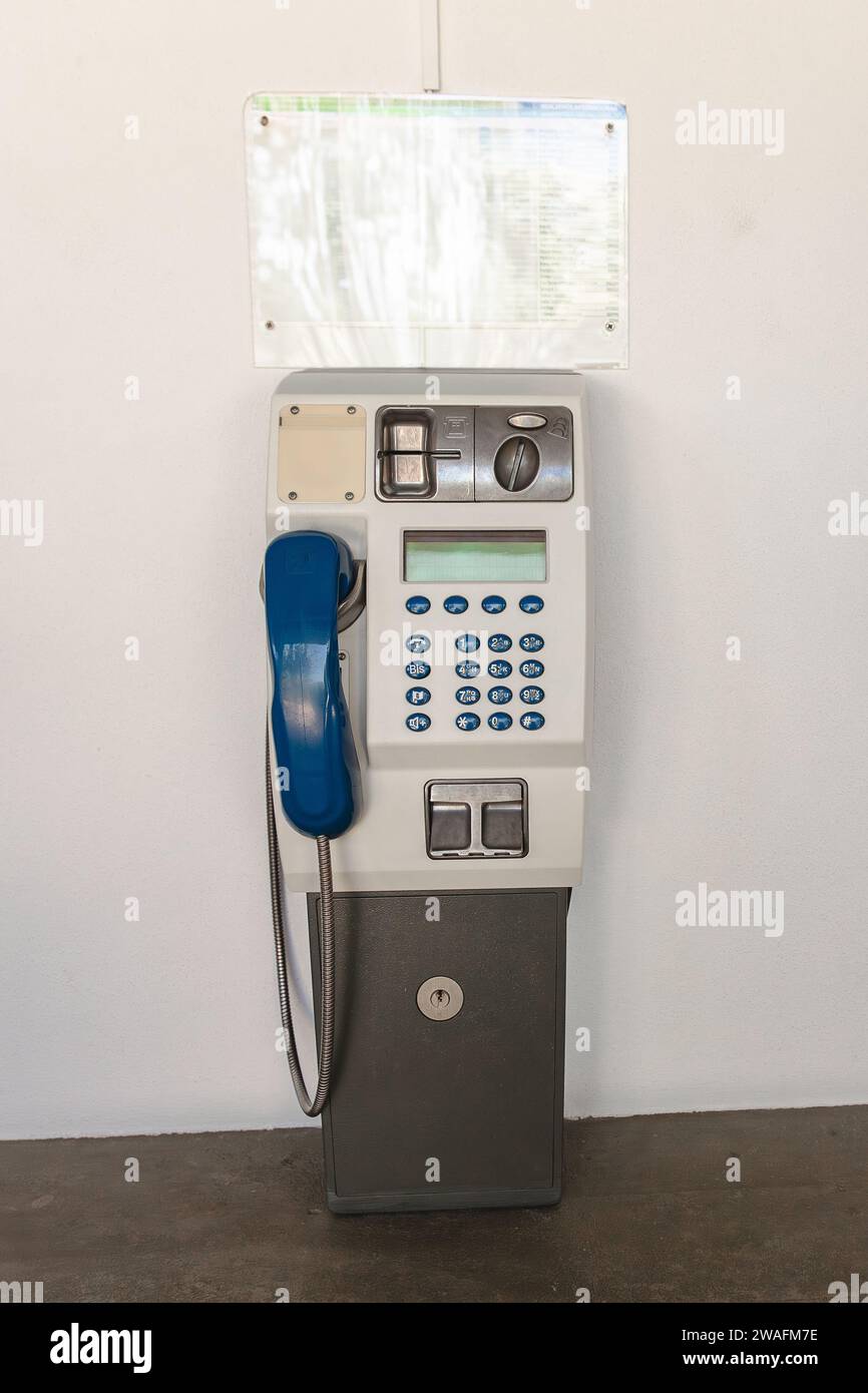 Old public telephone for making voice calls using coins or prepaid card stuck on a white wall. Stock Photo