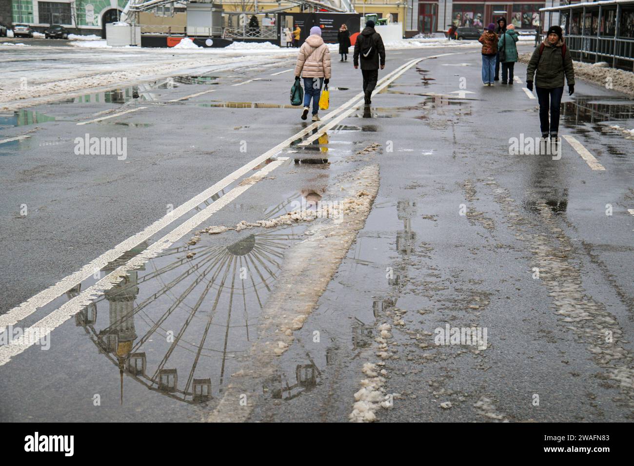 Non Exclusive KYIV UKRAINE JANUARY 4 2024 People Are Seen In   Non Exclusive Kyiv Ukraine January 4 2024 People Are Seen In Kontraktova Square As A Ferris Wheel Is Reflected In A Puddle In Winter Kyiv Cap 2WAFN83 