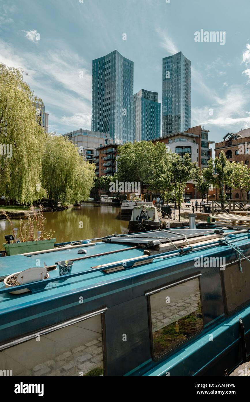 A cluster of skyscrapers stand tall above the Manchester canal basin. City living, high rise apartments and houseboats. Lifestyle, Travel or Tourism. Stock Photo