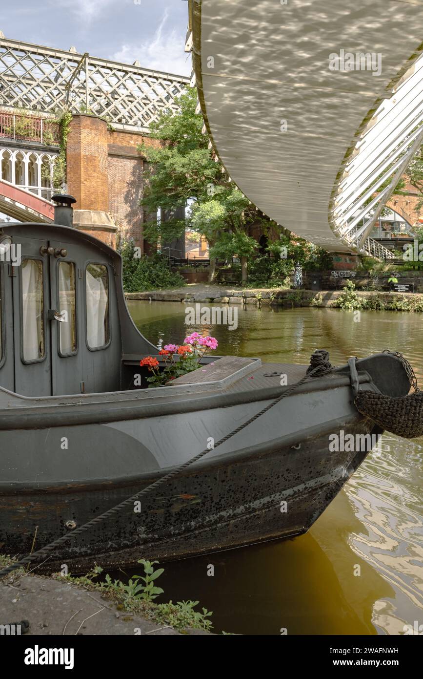 A moored houseboat with a footbridge overhead and Victorian railway bridge behind capture the charm of this tourism hotspot in Castlefield, Manchester Stock Photo