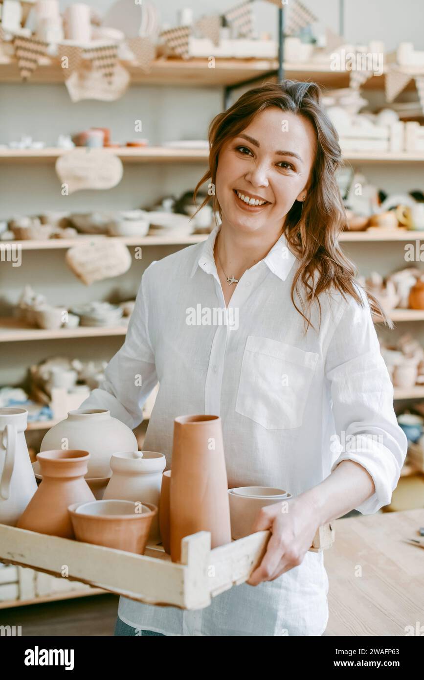 A female potter holds a box with raw clay products Stock Photo
