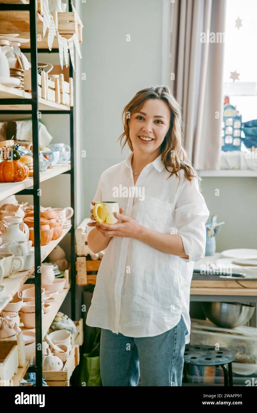 Beautiful middle-aged woman stands at shelf with pottery items Stock Photo