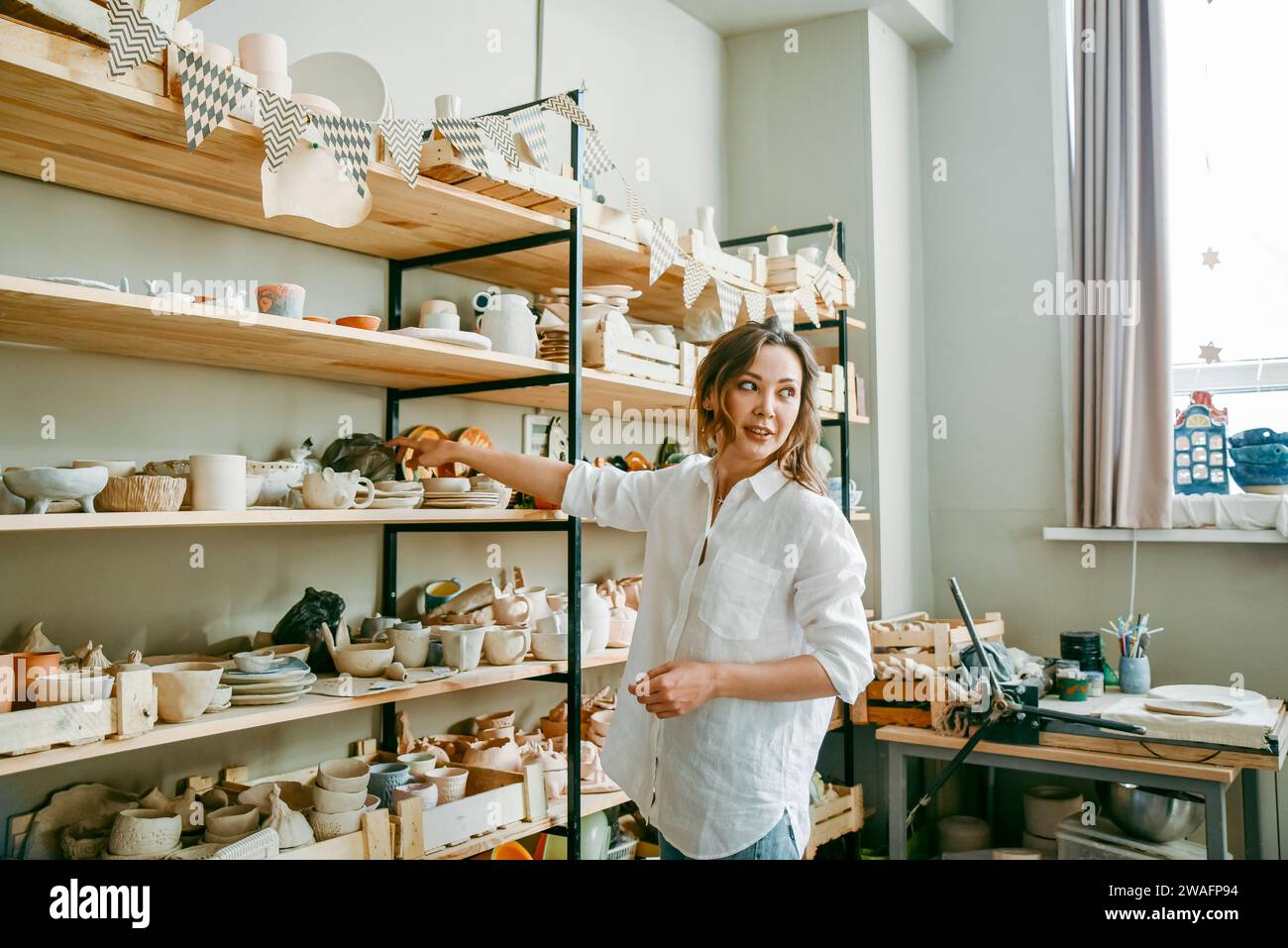 A woman head of pottery workshop near shelves with products Stock Photo