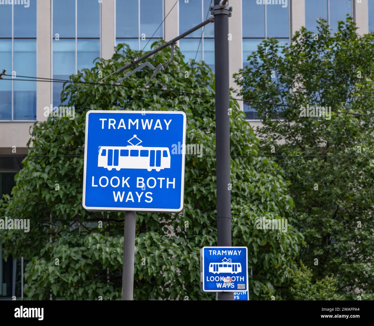 A UK street sign advising pedestrians to look both ways.at a tramway. A blue road sign advising of a tramway. Stock Photo