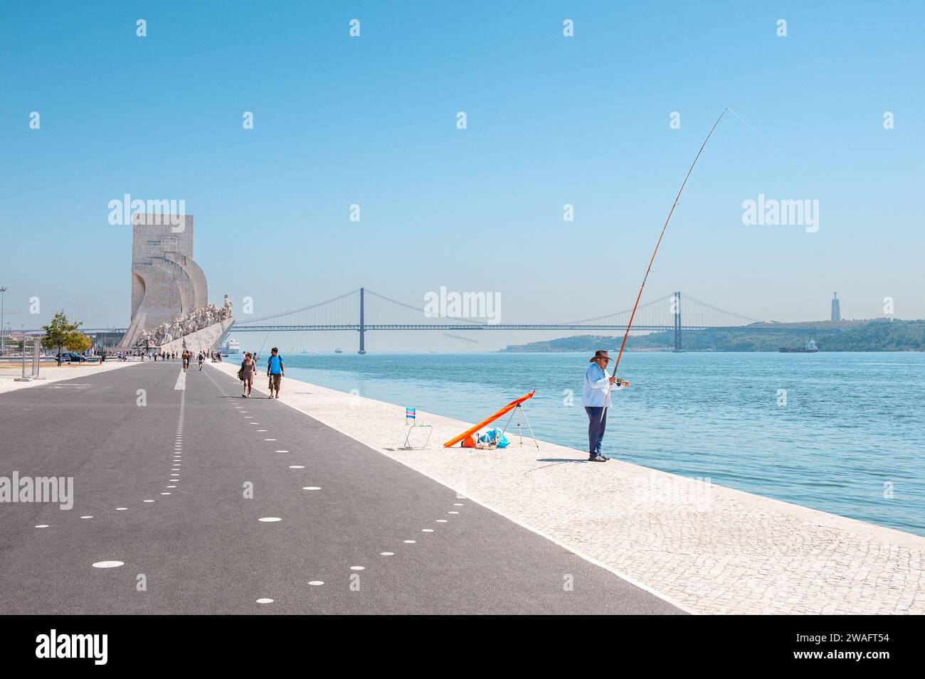 A lone fisherman with the  Monument to the Discoveries in the distance on Lisbon's Belem waterfront Stock Photo