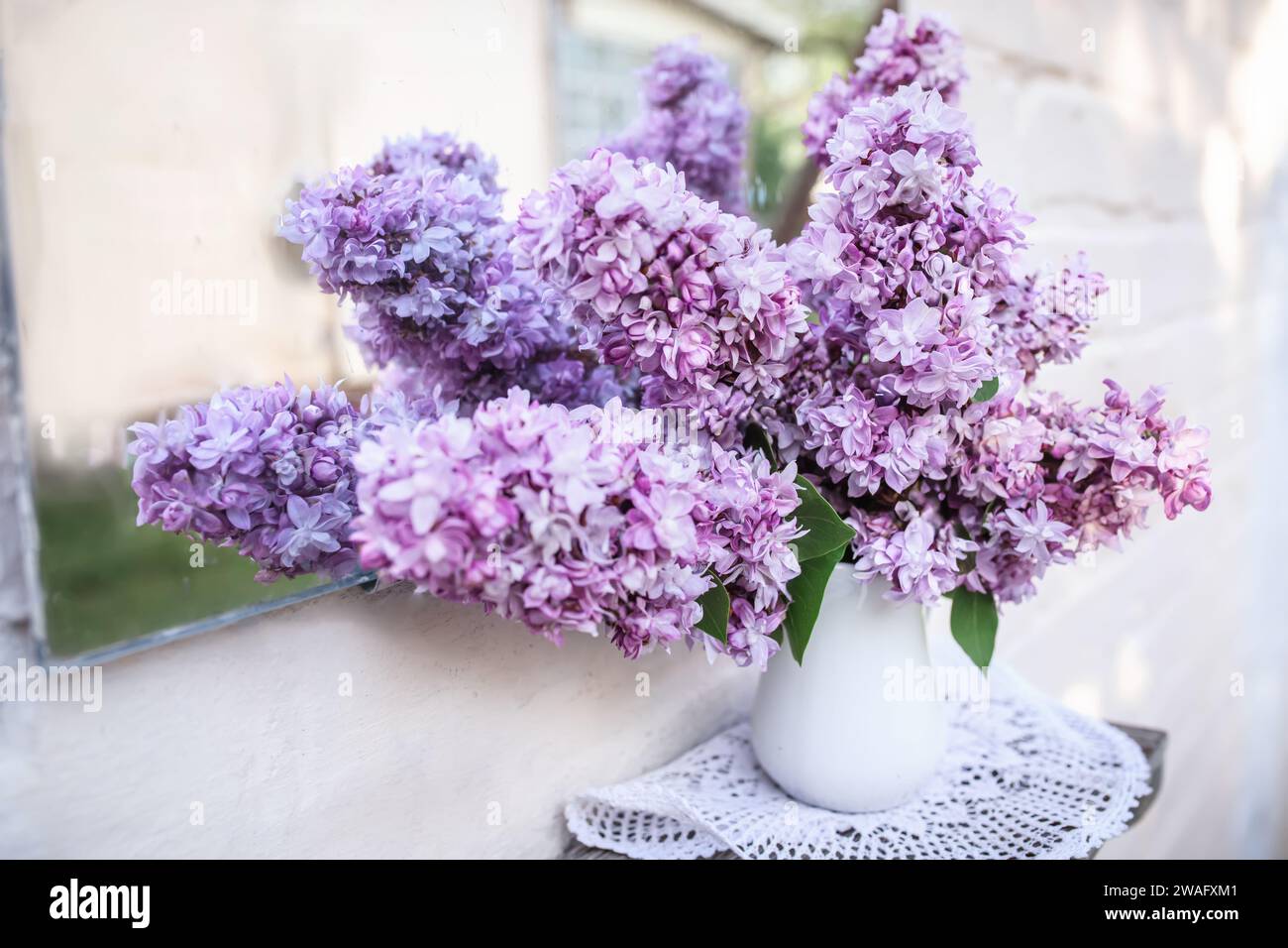 Bouquet of purple lilacs on a shelf near a vintage mirror. Reflection of flowers and courtyard in an old mirror. Home decor with spring flowers.. Stock Photo