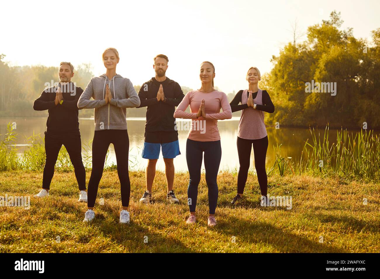 Group of fit and active people doing yoga exercises in nature. Outdoors fitness concept. Stock Photo