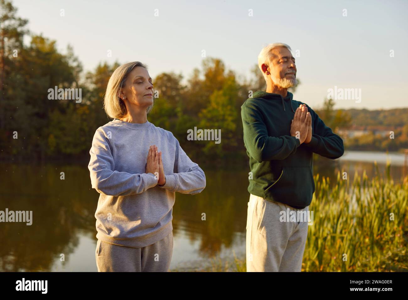 Active senior couple doing yoga exercises in nature. Outdoors fitness concept. Stock Photo
