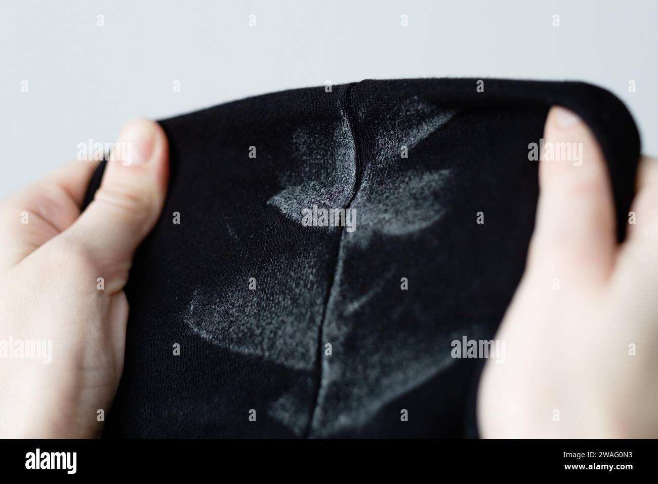 A woman's hand is showing white marks on deodorant stains in black clothes. Spoiled clothes. daily life stain concept. Stock Photo