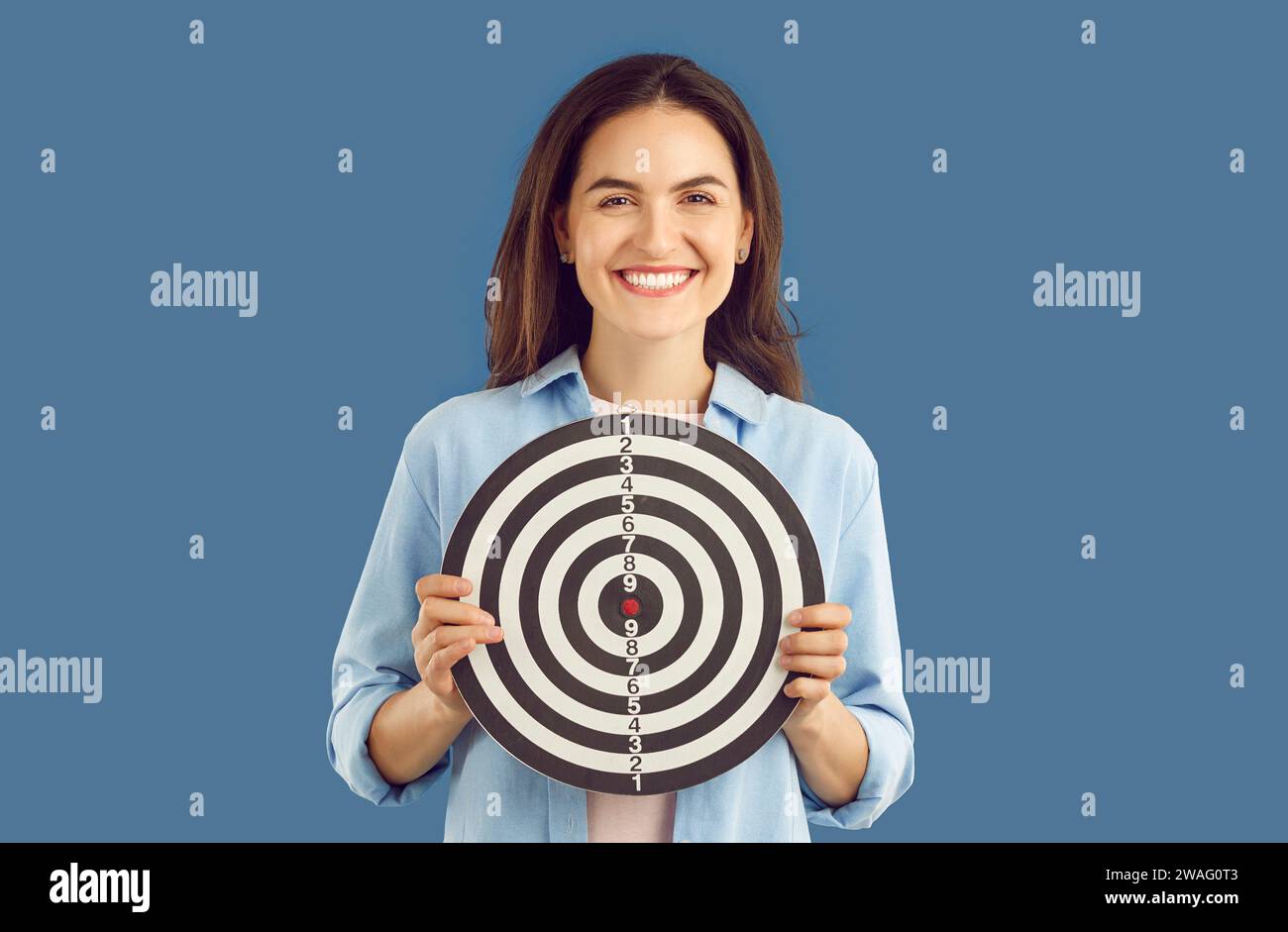 Positive smiling brunette woman in casual shirt holding darts shooting ...