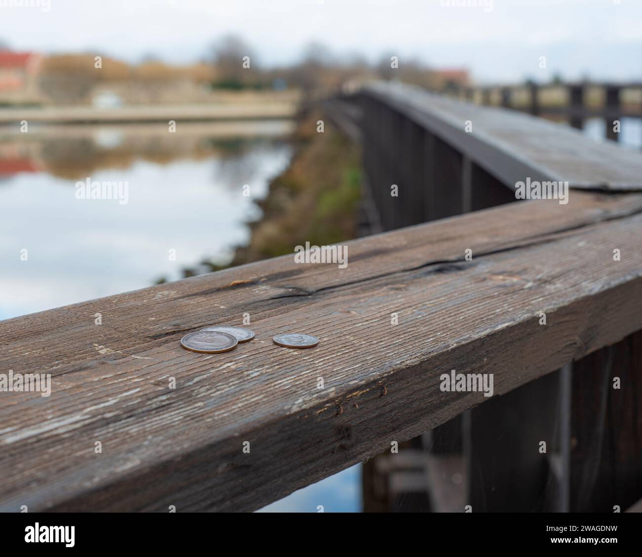 An aged wooden railing by a river is adorned with coins protruding from the top, creating a rustic, aged look Stock Photo
