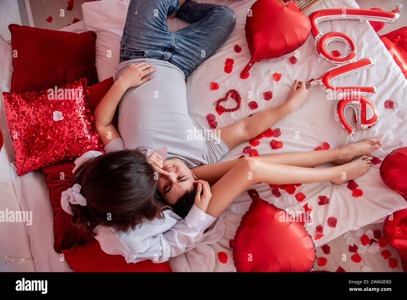 Top view of loving couple in casual clothes on white bed with red heart ...