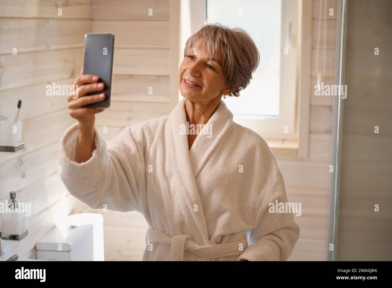 Pleasant lady in a bathrobe takes a selfie in bathroom Stock Photo - Alamy