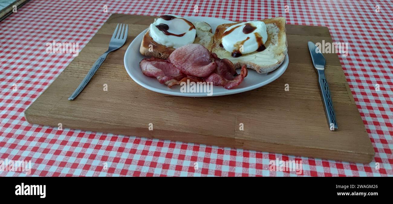 Breakfast on a plate. Poached eggs, toast, bacon and some brown sauce, on a plate, using a cutting board as a tray. Stock Photo