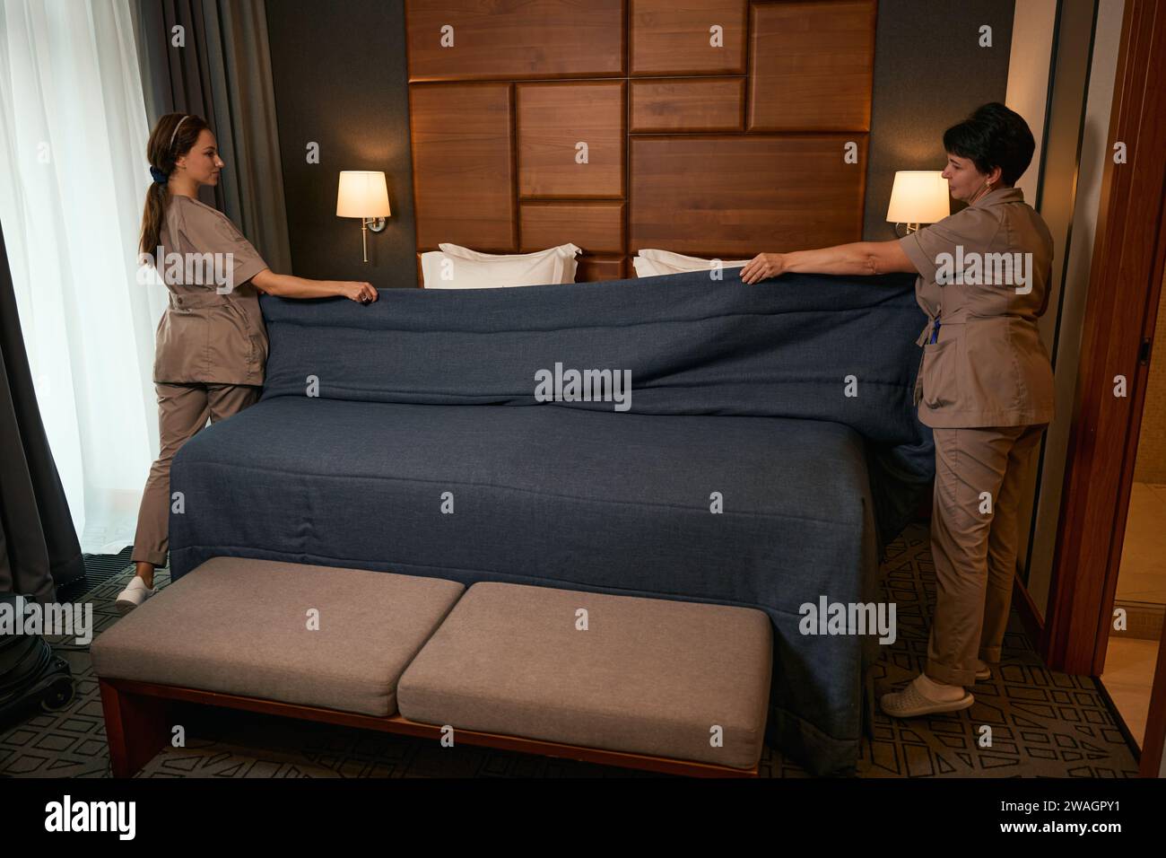 Team of chambermaids busy with bedmaking procedure in hotel room Stock
