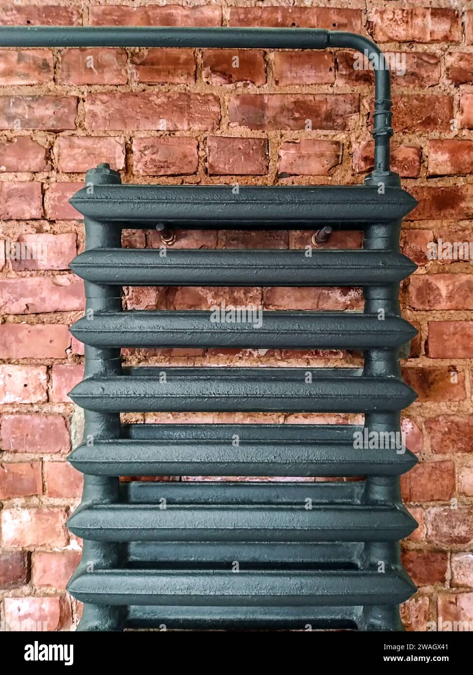 A part of an indoor Cast-iron water heating battery, radiator on the red brick wall Stock Photo