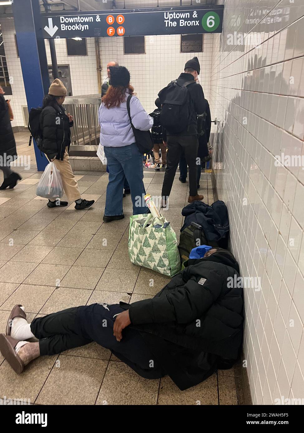 Homeless man with his belongings sleeps within the Bleeker Street subway station in Manhattan as riders transfer train lines. Stock Photo