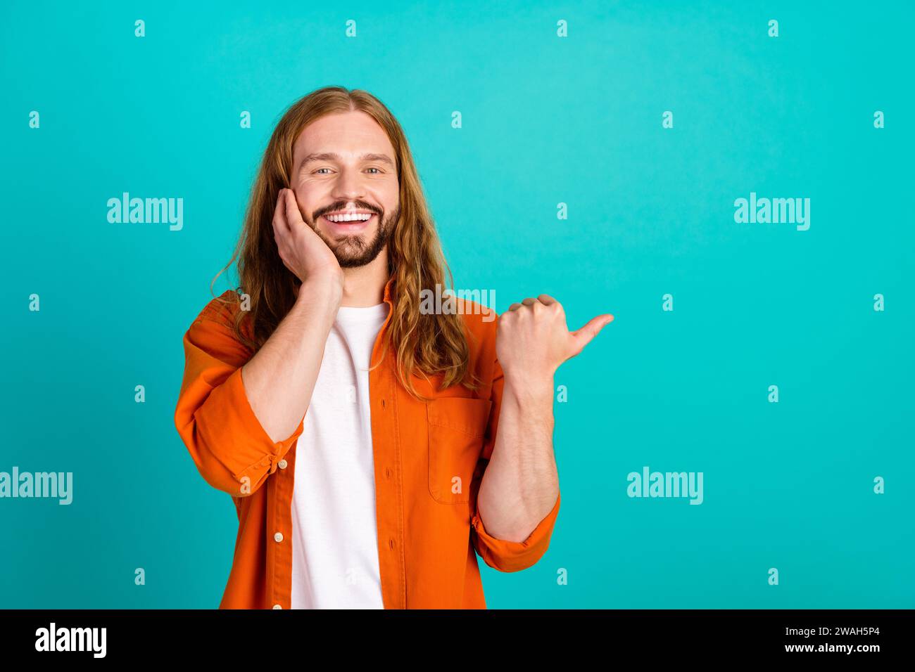 Photo of optimistic young hippie guy in orange shirt point thumb empty ...