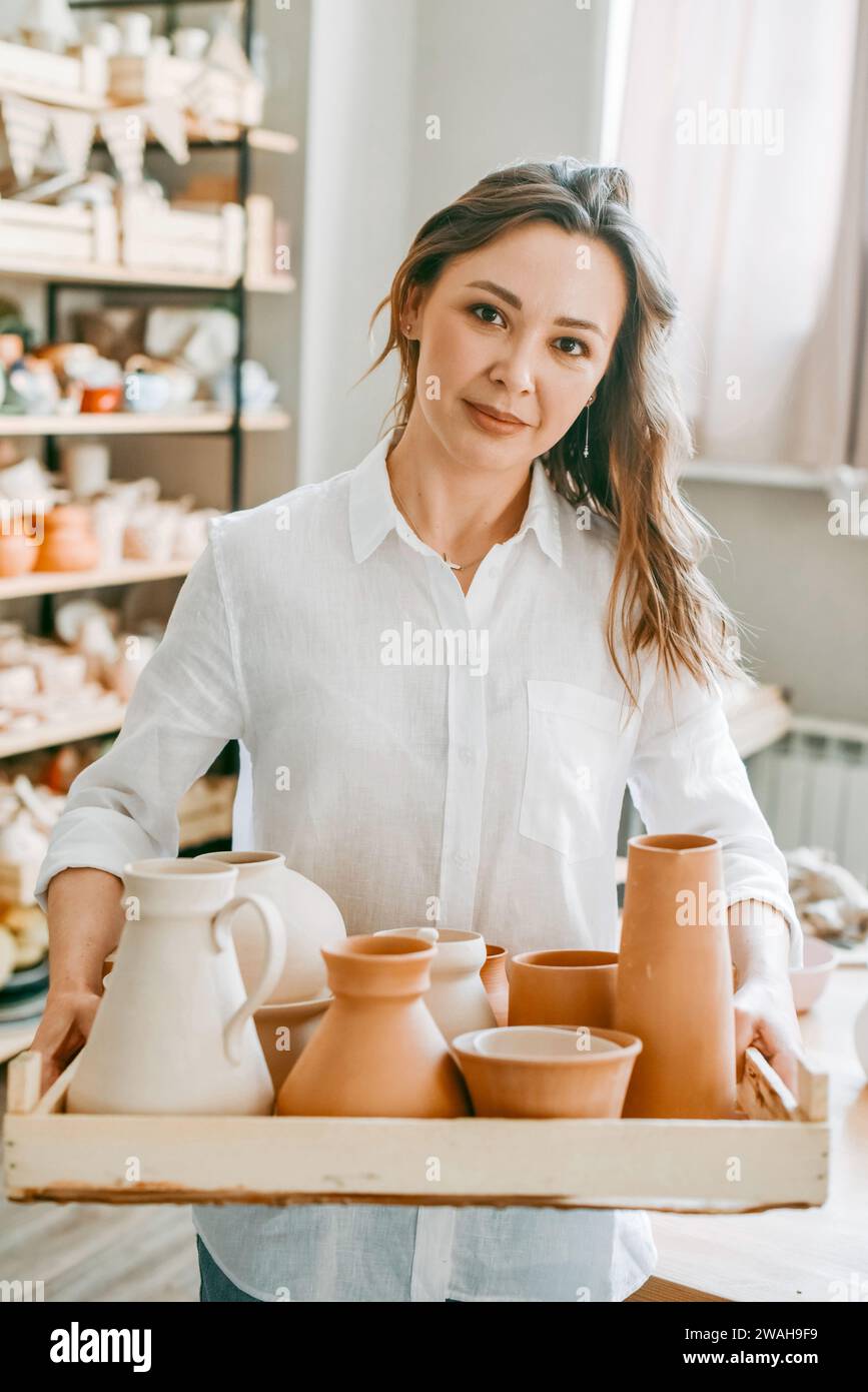 Woman master of pottery workshop carries clay products for firing Stock Photo