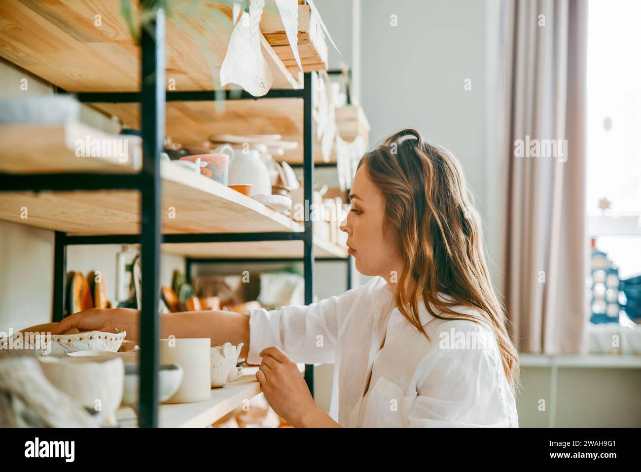 A woman head of pottery workshop near shelves with products Stock Photo