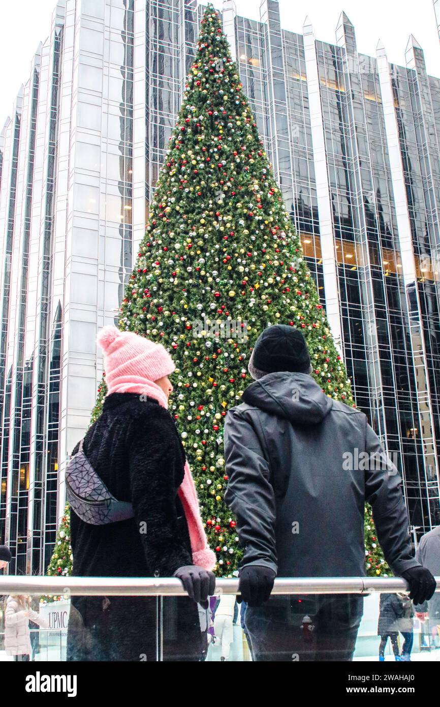A couple dressed in their winter clothing look on at the Christmas Tree lit up in the center of PPG Arena ice rink Stock Photo
