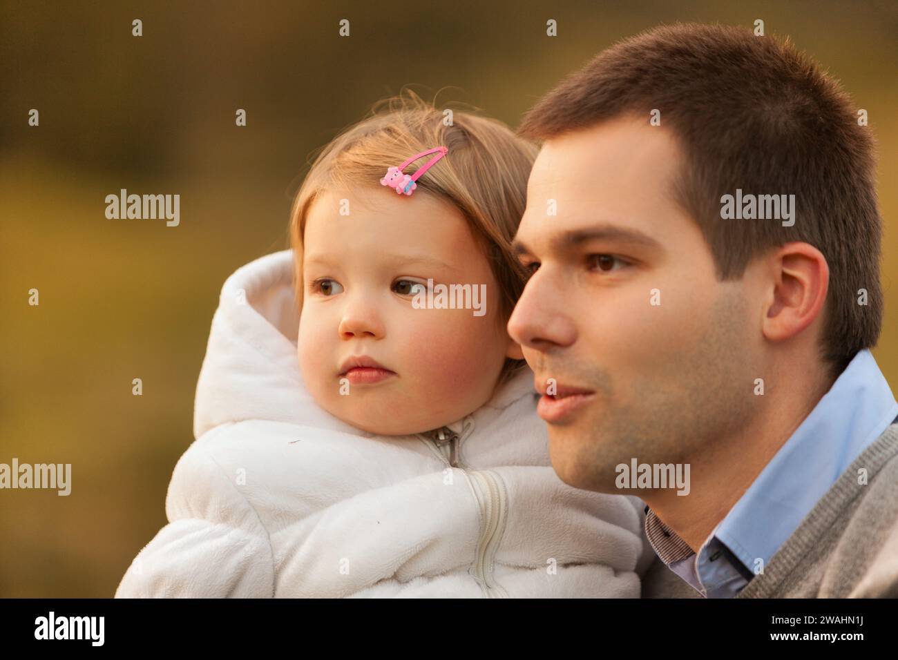 Tender moment captured as father holds young daughter in his arms, their expressions serene against a soft-focus background Stock Photo