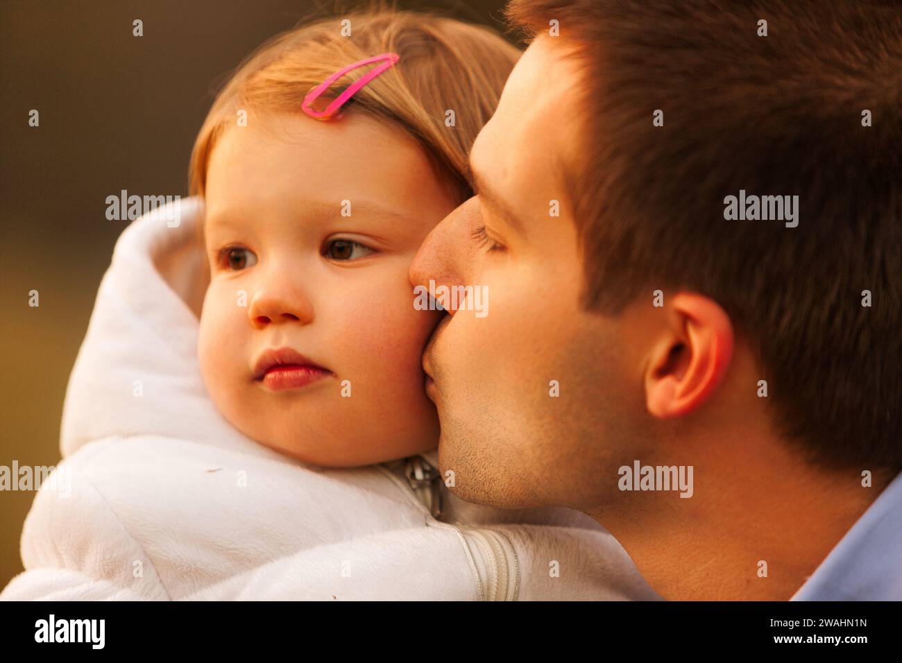 With a gentle kiss on the cheek, the father cherishes a quiet moment with his contemplative young daughter Stock Photo