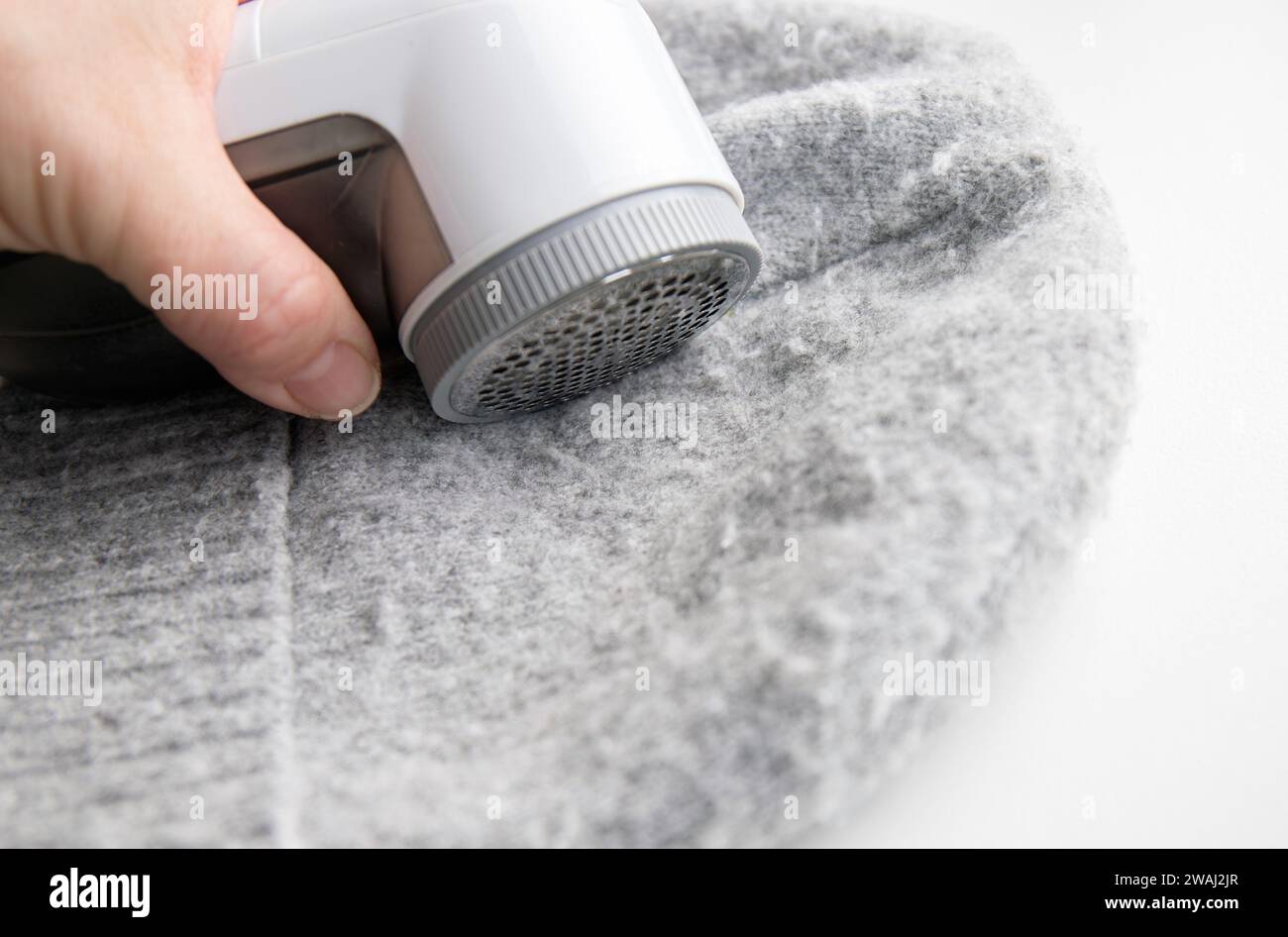 Person hand using sheaving lint balls from winter hat with lint shaver machine tool. Clothes maintenance concept. Stock Photo