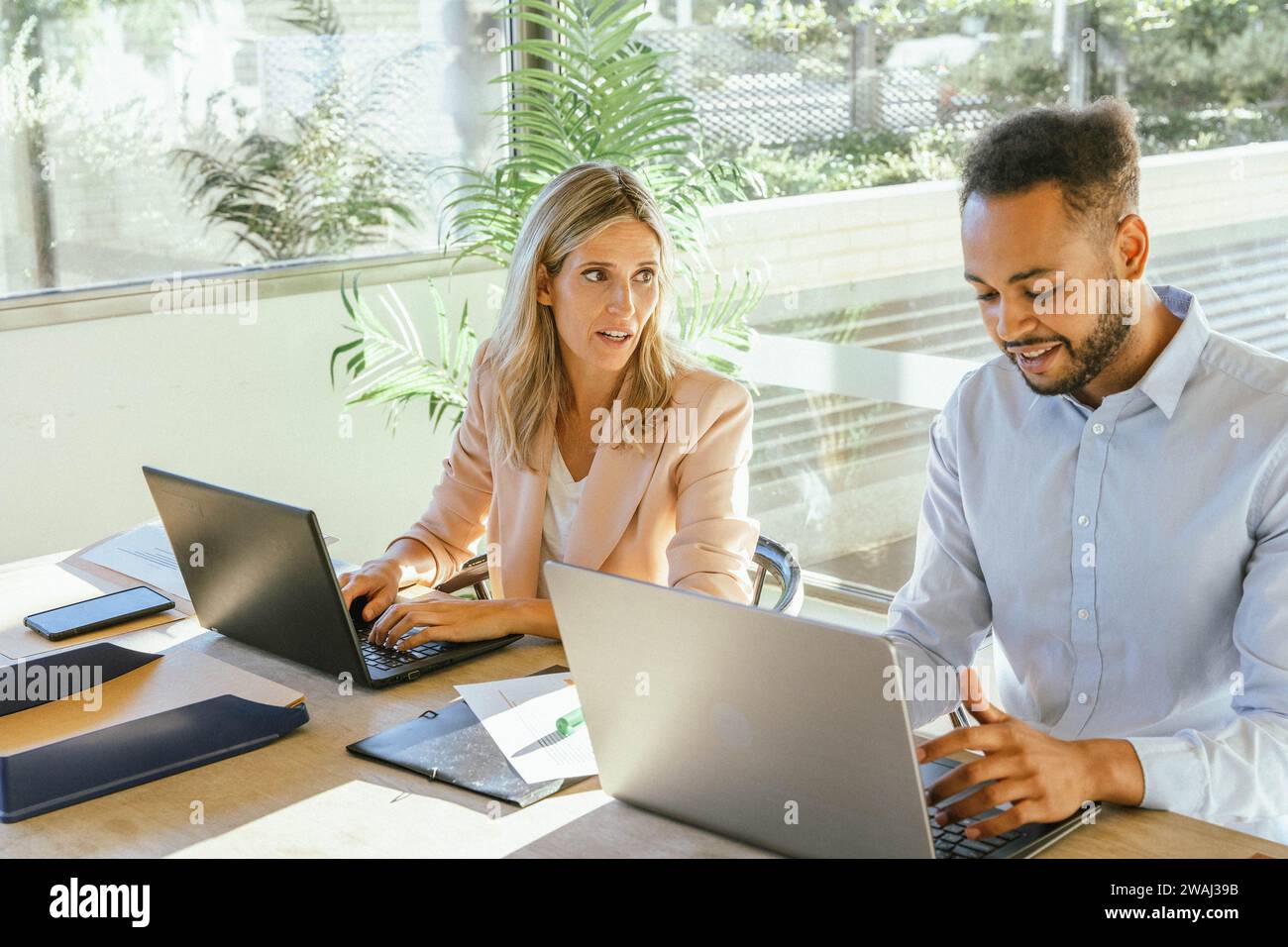 Two business co-workers talking while working with their computers at the office. Business concept. Stock Photo