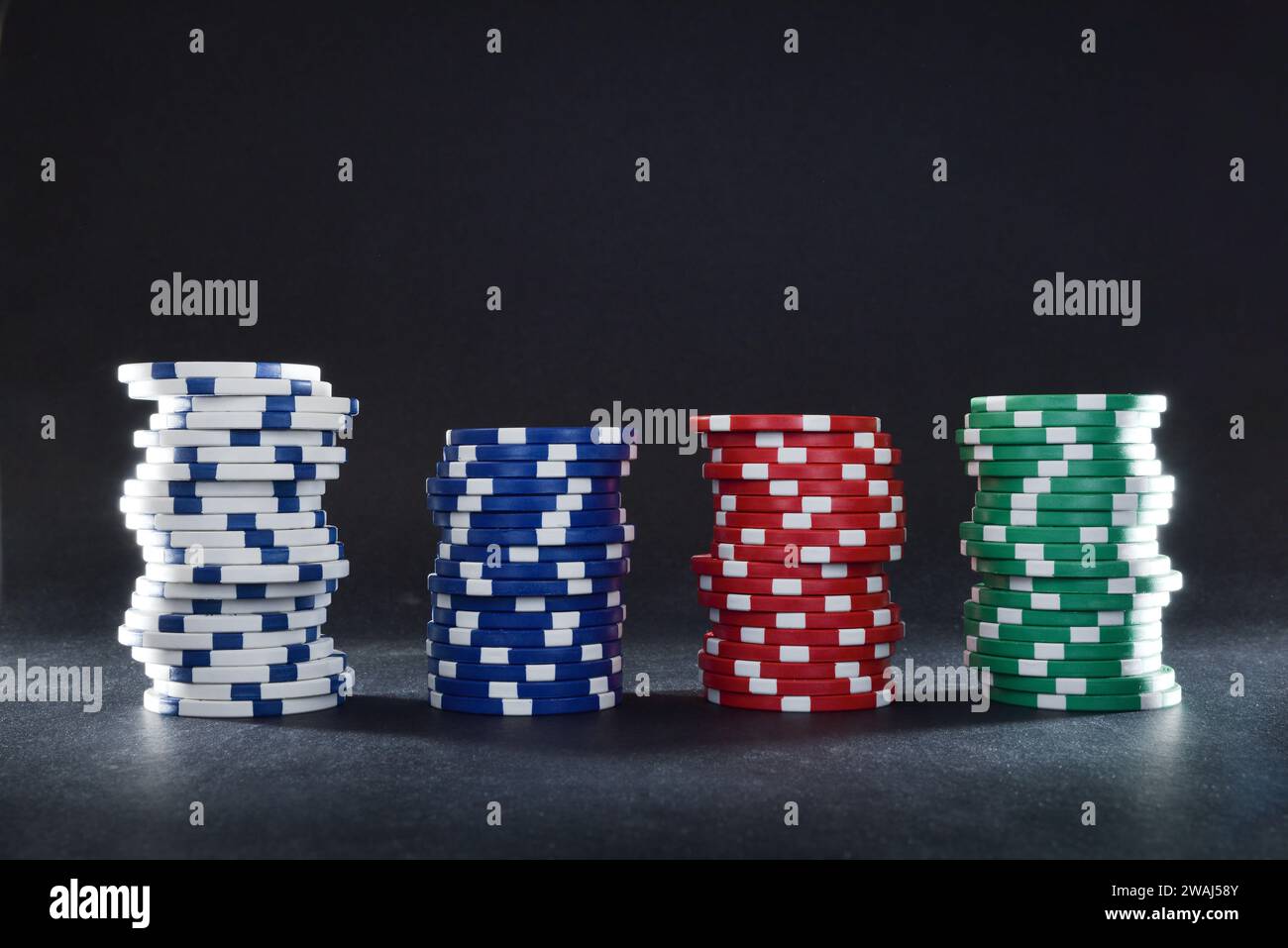Various stacks of casino game bet chips of various colors on black table and black isolated background. Front view. Stock Photo