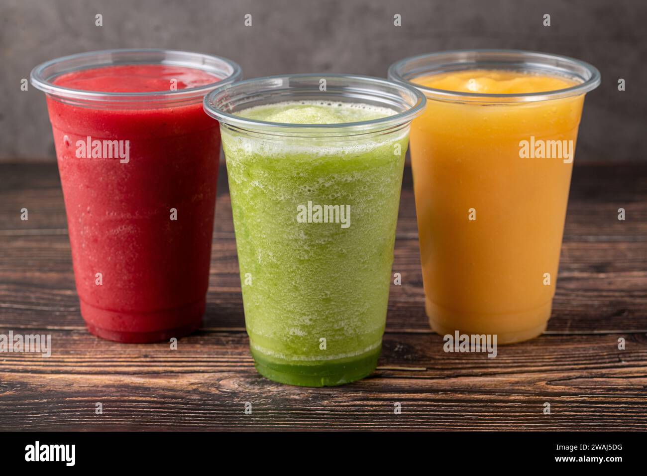 Three different fruit smoothies in plastic take away glasses on wooden background Stock Photo