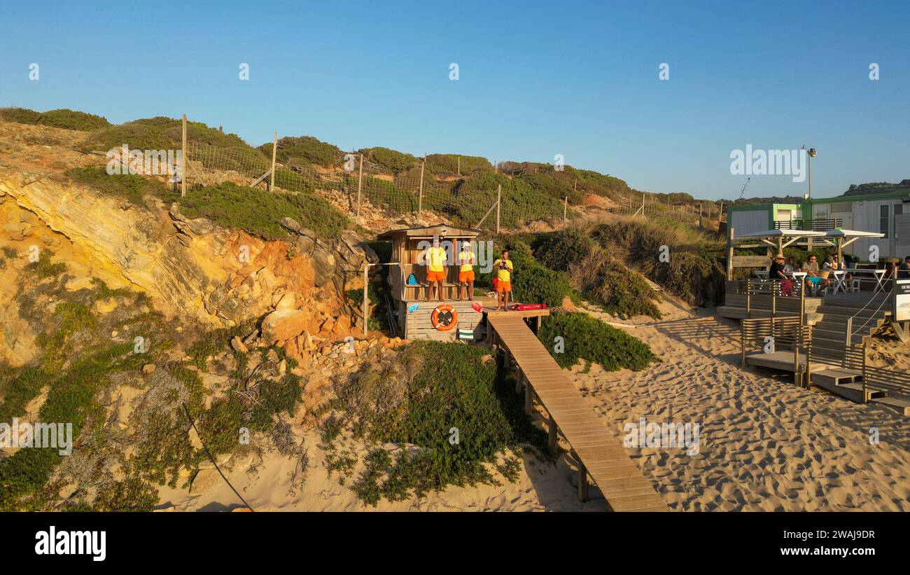 A close-up of a diverse group of people standing on a sandy beach near a wooden fence, Portugal Stock Photo