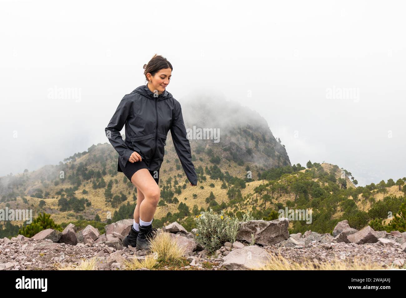 An active woman trail running on a rugged path in Cumbres del Ajusco National Park with the misty Pico del Aguila in the background Stock Photo