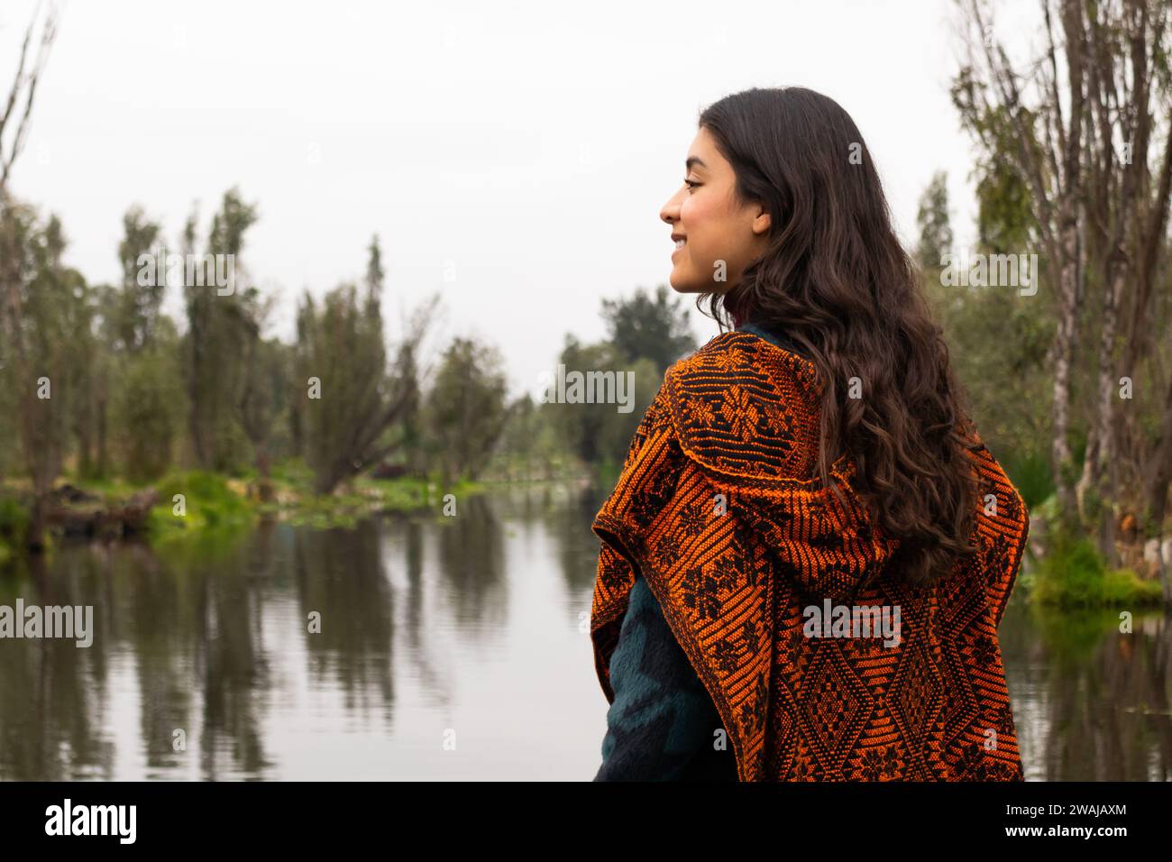 Side view of woman in a patterned shawl looks out over the peaceful waters of Xochimilcos canals Stock Photo