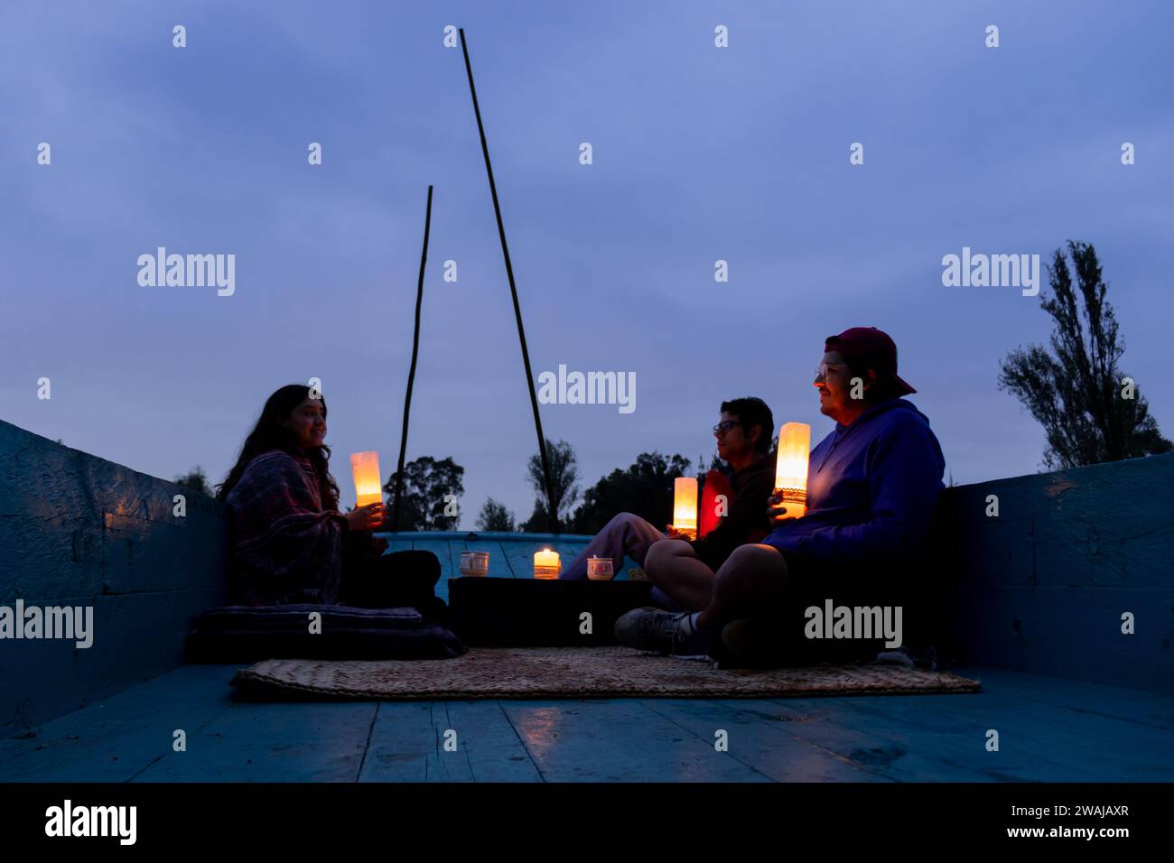 Three individuals are engaging in a serene twilight experience in Xochimilco Mexico City surrounded by lanterns that cast a soft glow Stock Photo