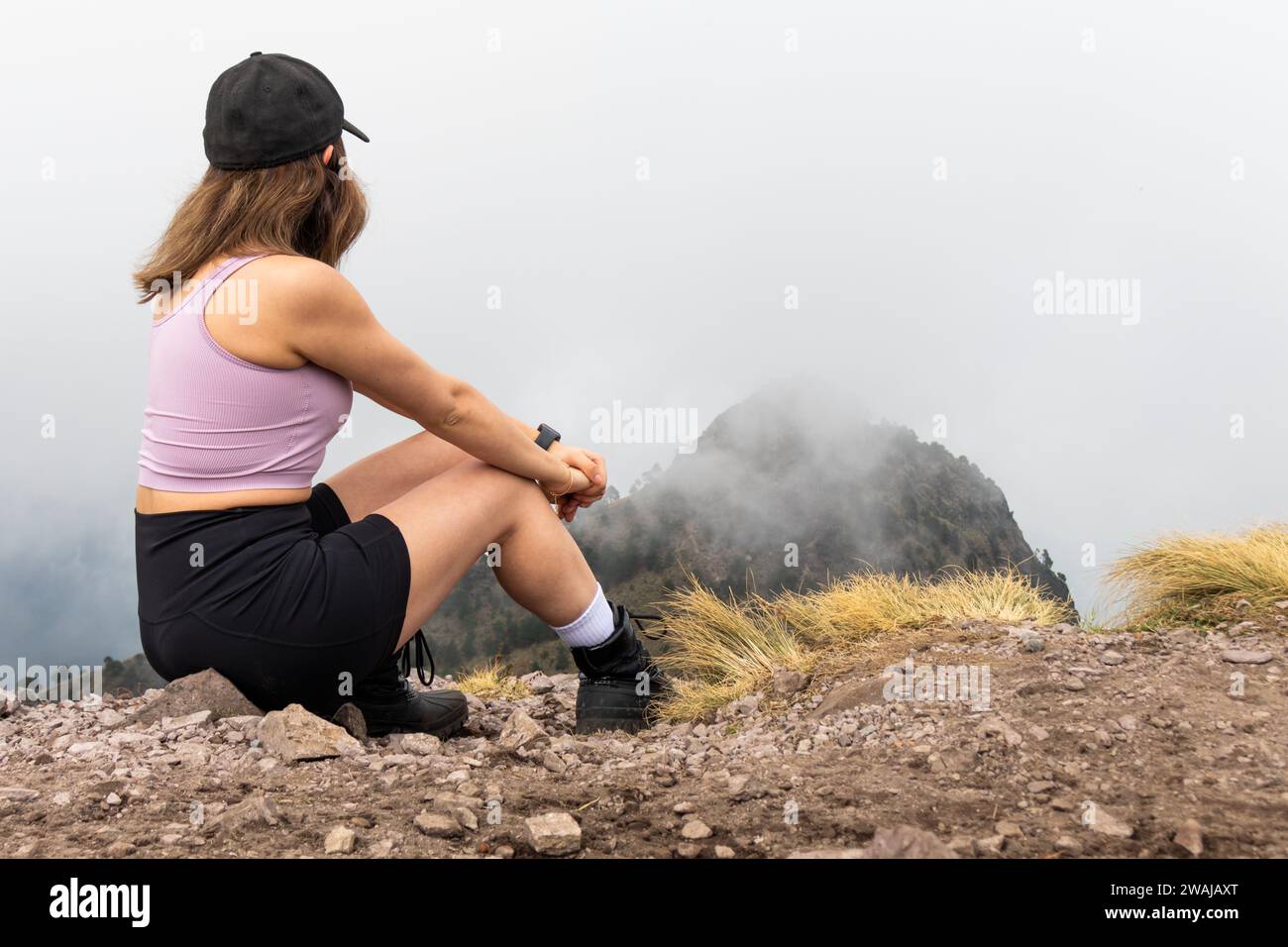 Anonymous reflective hiker sitting and looking out at the fog enveloped summit of Pico del Aguila from the heights of Cumbres del Ajusco National Park Stock Photo